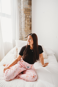 Thumbnail for Female model sitting on white bed looking off into the distance smiling wearing Hogs And Kisses pajama lounge pants