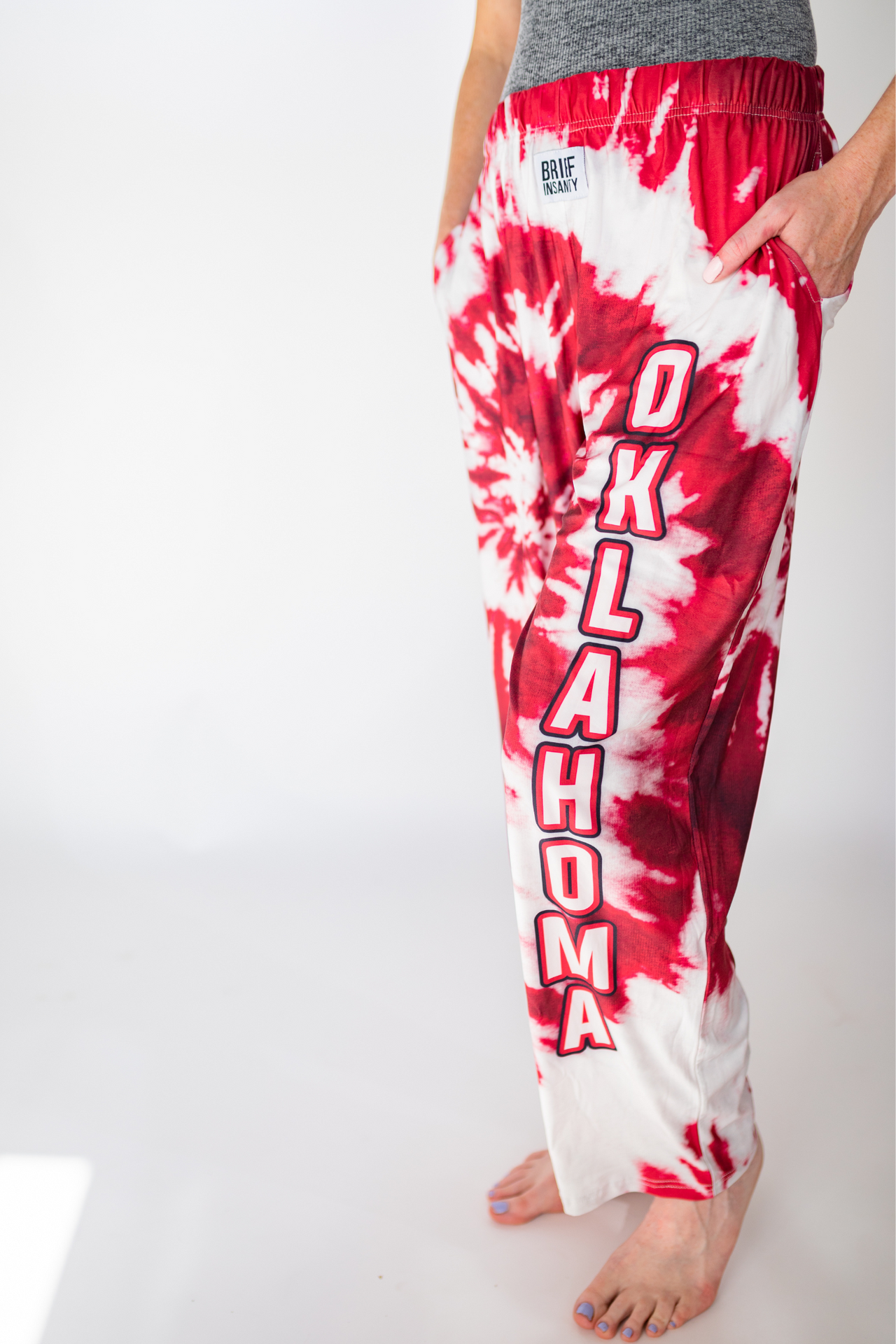 Waist down photo of model wearing Oklahoma Red Tie-Dye pajama lounge pants front/side angle view (white background)