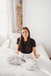 Thumbnail for Female model sitting on white bed facing forward and smiling wearing Just Screw It Wine pajama lounge pants
