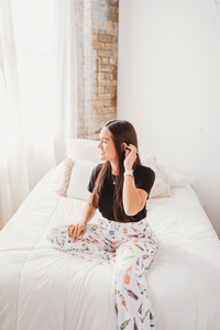 Thumbnail for Female model sitting on white bed looking off to the side and smiling wearing Just Screw It Wine pajama lounge pants