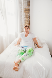 Thumbnail for Male model sitting on a white bed facing forward with legs stretched out wearing Golf With A Chance Of Beer pajama lounge pants