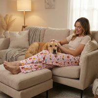 Thumbnail for Female model relaxing on sofa wearing dog-themed lounge pants gently petting a dog, cozy living room scene.