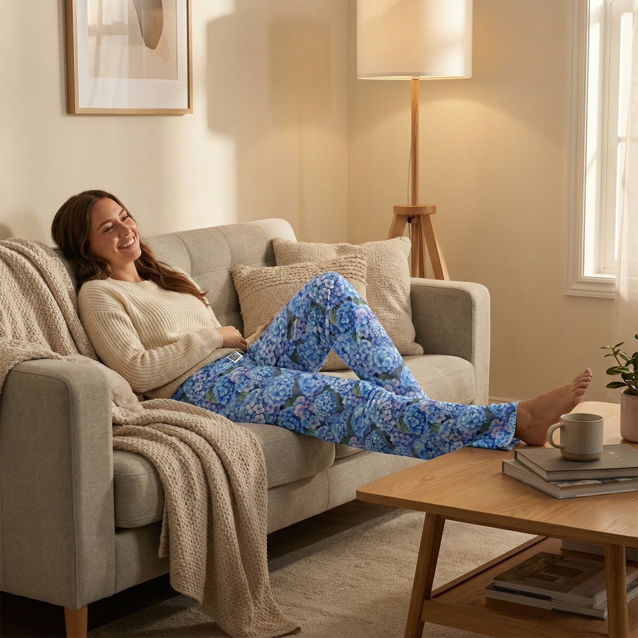 Female model wearing Blue Hydrangea Lounge Pants, relaxing on a modern couch in a cozy living room.