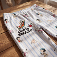Thumbnail for Close-up of Snoopy beach-inspired lounge pants on wooden surface, showcasing vibrant 'Life Is Beachy' graphic and breezy striped fabric.
