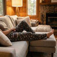 Thumbnail for Model relaxing on a modern couch in a cozy cabin, showcasing Snoopy Outside Life lounge pants with woodland and campsite print.