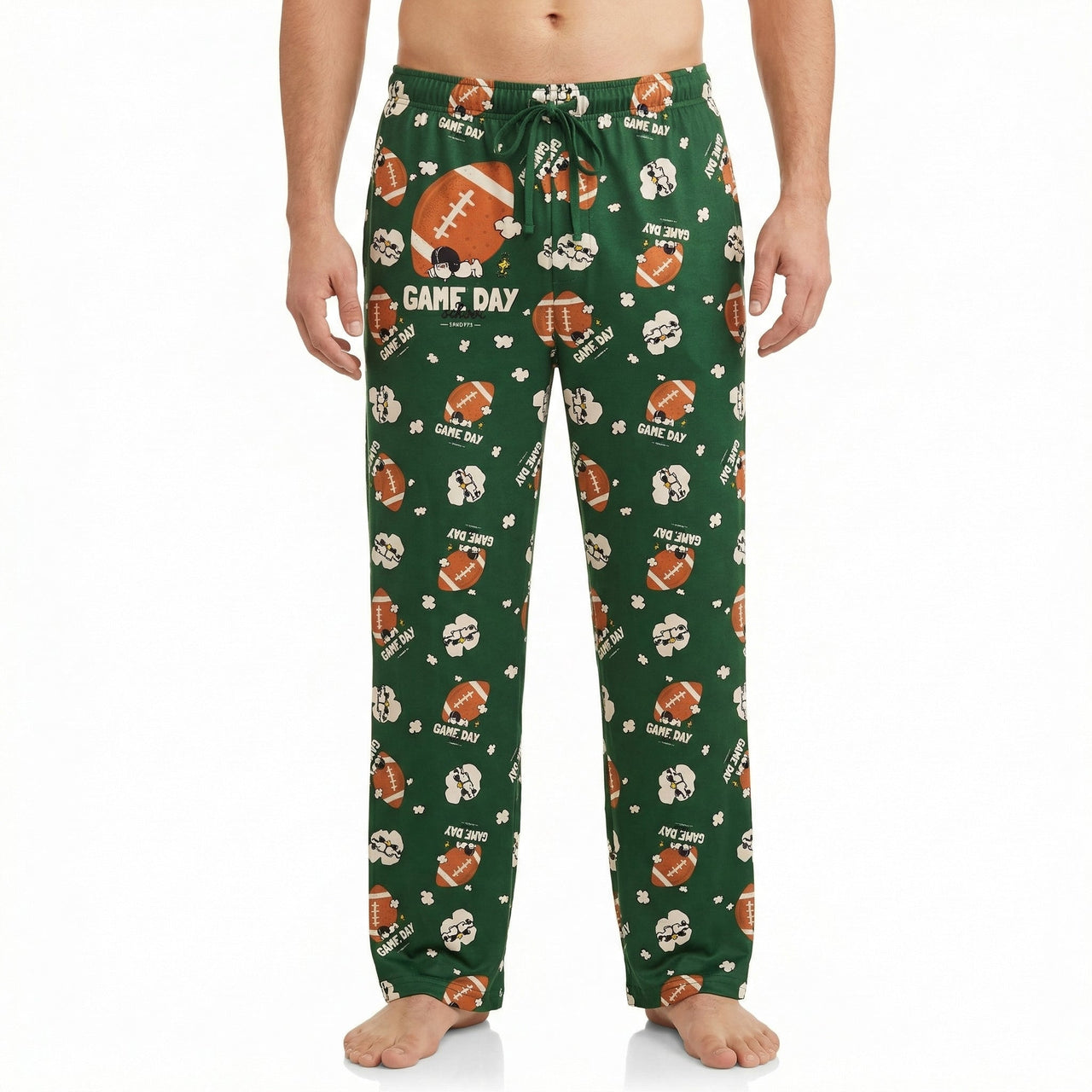 Model wearing green football-themed lounge pants featuring Snoopy and game day graphics, cropped from waist to ankles against white background.